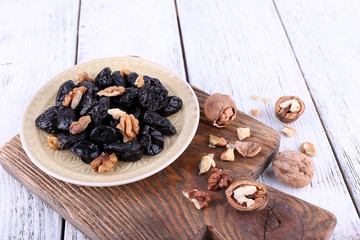 Wooden board with plate of prunes and walnuts