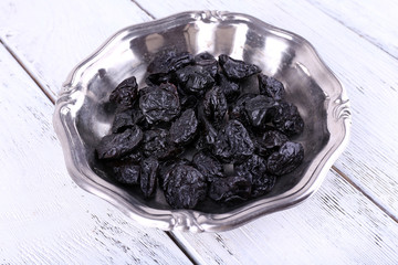 Metal plate of prunes on color wooden background