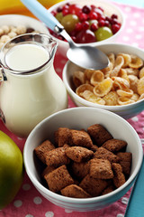 Various sweet cereals in ceramic bowls, fruits and jug with