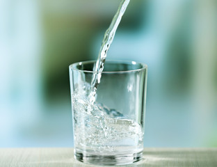 Pouring water from bottle on  glass on light background