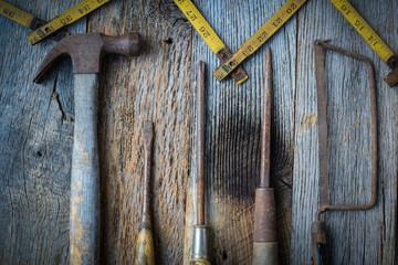 Hammer, Screwdriver, Hand Saw and Tape Measure on Rustic Wood Ba
