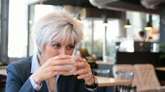 business middle aged woman drinks coffee in cafe and smiles