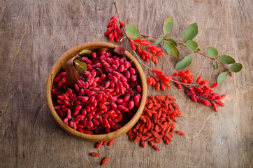 Barberry with leaves and dry goji berries on wooden background