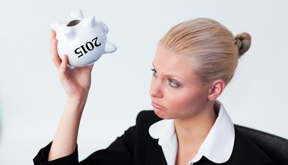 Composite image of sad business woman looking into piggy bank
