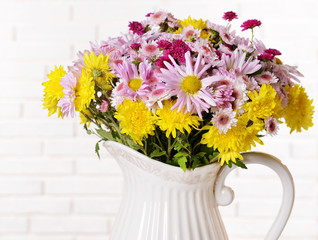Beautiful flowers in pitcher on table on light background
