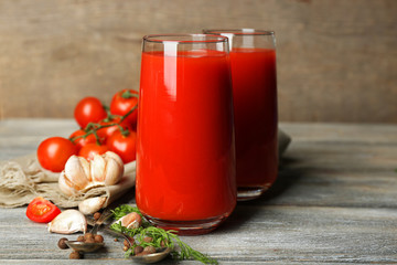 Glasses of tasty tomato juice and fresh tomatoes on wooden
