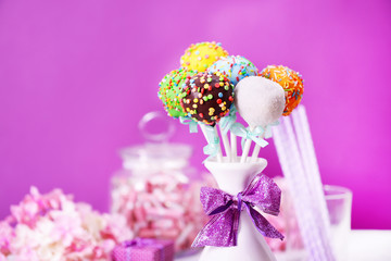 Sweet cake pops in vase on table on purple background