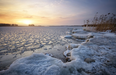 Beautiful winter landscape with frozen lake and sunset sky.