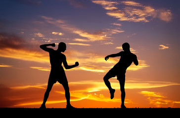 Silhouettes of two fighters on sunset fiery background