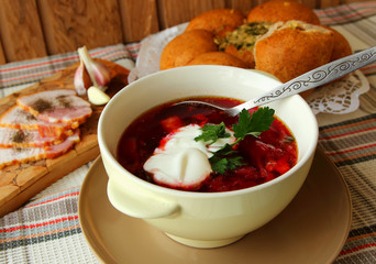 A plate of hot borscht with sour cream, bread and meat.