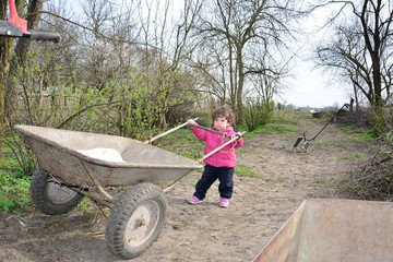 In the spring of small rural girl carries a wheelbarrow.