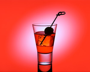 Short drink glass with red liquid and green olive