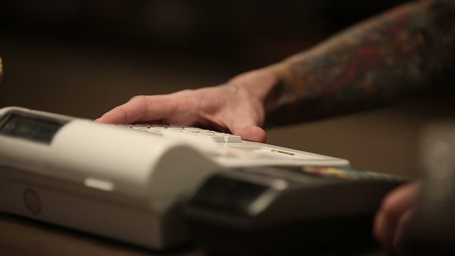 Seller man with tattoos on his hands and cash register