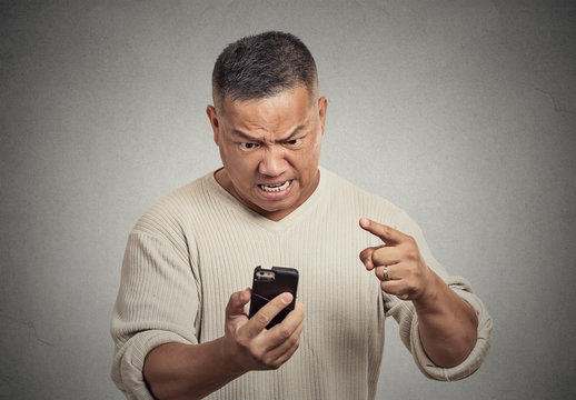 angry middle aged man while on mobile, pointing at smart phone