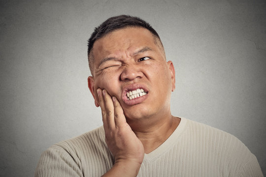 man touching face having bad pain, tooth ache grey background 