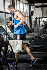 Young man running at treadmill in gym