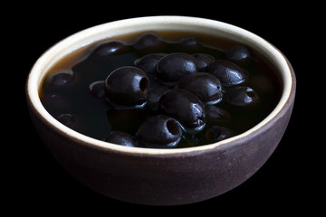 Ceramic rustic bowl of black olives on black surface.
