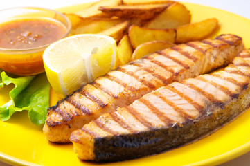 Grilled salmon steak with potatoes and sauce on a yellow plate