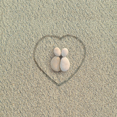 Pebbles shapes lovers with heart on the sand