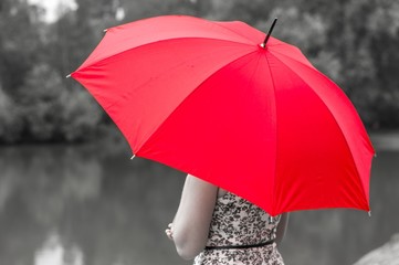 Girl with red umbrella stands near the pond