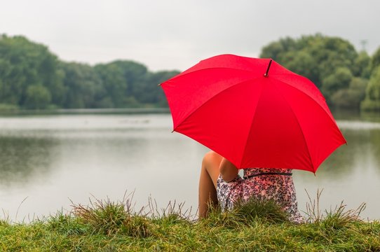 Girl With Red Umbrella Sits Near The Pond