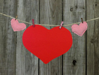 Red hearts hanging on clothesline by wood fence