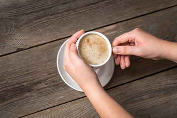 Womans hands holding hot cup of coffee. View from top on a mug