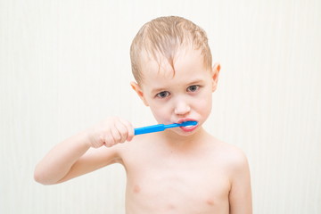 Blonde beautiful boy brushing his teeth in the bathroom