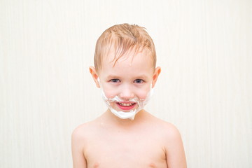 Little boy in bath with a mustache and a beard of foam
