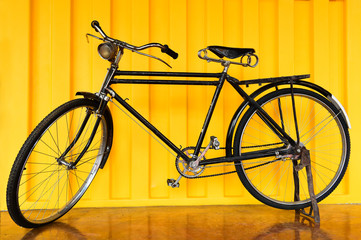 Old vintage black bicycle on yellow background.