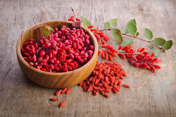 Barberry with leaves and dry goji berries on wooden background