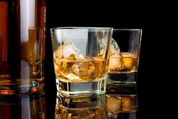 whiskey with ice in glasses near bottle on black background