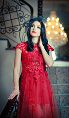 The beautiful girl in a long red dress posing in a vintage scene