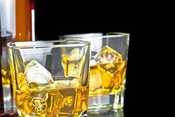 whiskey with ice in glasses near bottle on black background