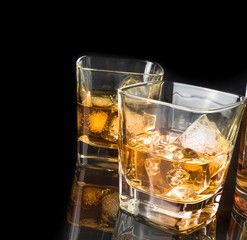 whiskey with ice in glasses near bottle on black background