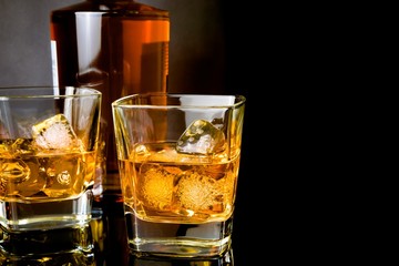 whiskey in glasses in front of bottle on black background