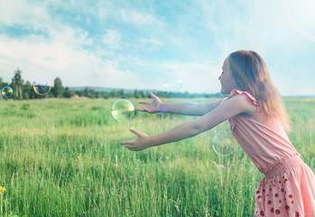 Girl playing among soap bubbles in summer