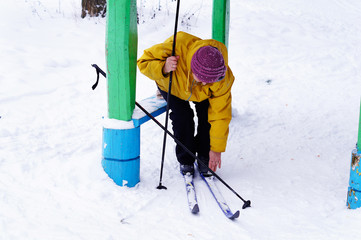 An old woman puts on skis in the forest