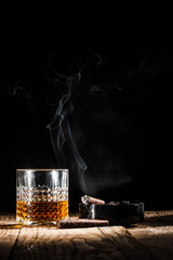 Glass of alcohol and smoking noble cigar on a black background