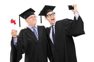 Senior and guy in graduation gowns taking a selfie