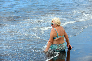 Aged woman on the wet black sand of Arena beach.