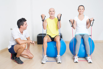 Obraz na płótnie Canvas Zwei Senioren beim Seiltraining auf Fitnessball mit Trainer