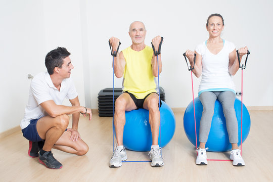 Zwei Senioren beim Seiltraining auf Fitnessball mit Trainer