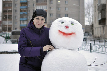 The woman near a snowman in the yard of the house.