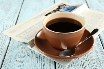 Cup of coffee with newspaper on color wooden background