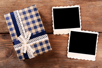 Obraz premium Gift box with blue gingham pattern and lace ribbon bow, two blank vintage photo frames on rustic wooden background