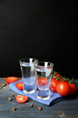 Glasses of ouzo and tomatoes on wooden table, on grey