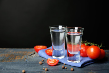 Glasses of ouzo and tomatoes on wooden table, on grey