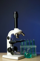 Microscope and test tubes on table, on color background