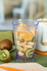 Sliced fruits and blender on wooden table, on bright background